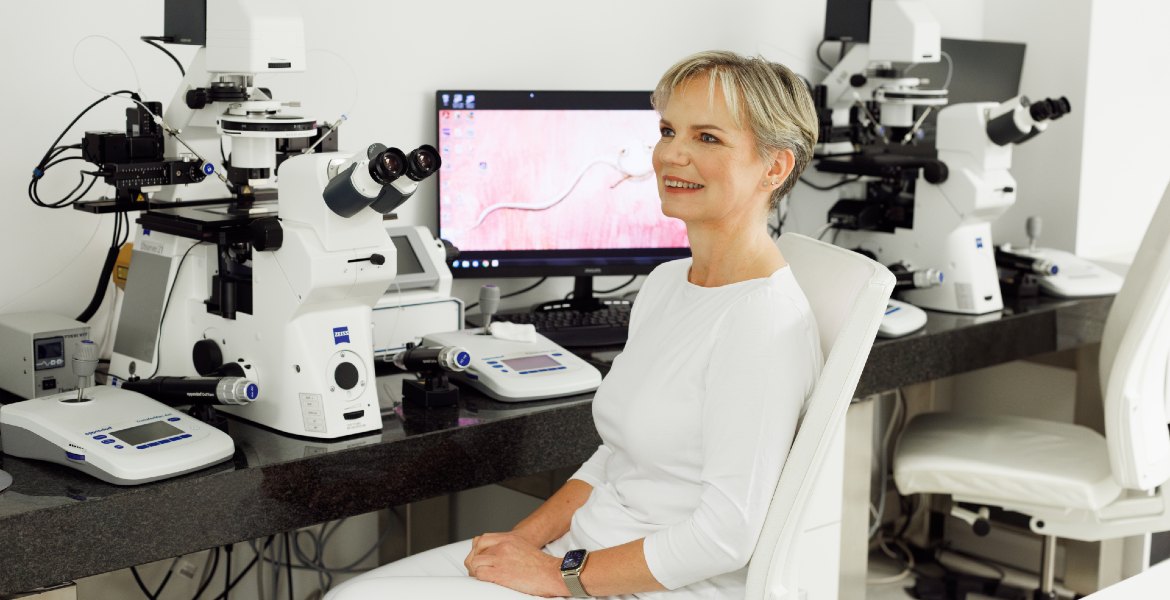 MSc Renata Hüttelova dans un laboratoire de FIV, assise à côté de microscopes et d’équipements de test de fertilité, appareils de marque Zeiss visibles sur le bureau.