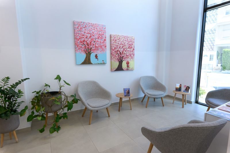Salle d'attente moderne à la Cryos IVF Clinic Chypre, dotée de fauteuils gris, de tableaux stylisés représentant des cerisiers en fleurs, de plantes d'intérieur et d'une lumière naturelle, reflétant un environnement accueillant et serein pour les patients.