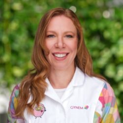 Dr Kristýna Fruhaufová sourit en blouse colorée GYNEM avec logo emoji rose, fond vert luxuriant, experte en fertilité.
